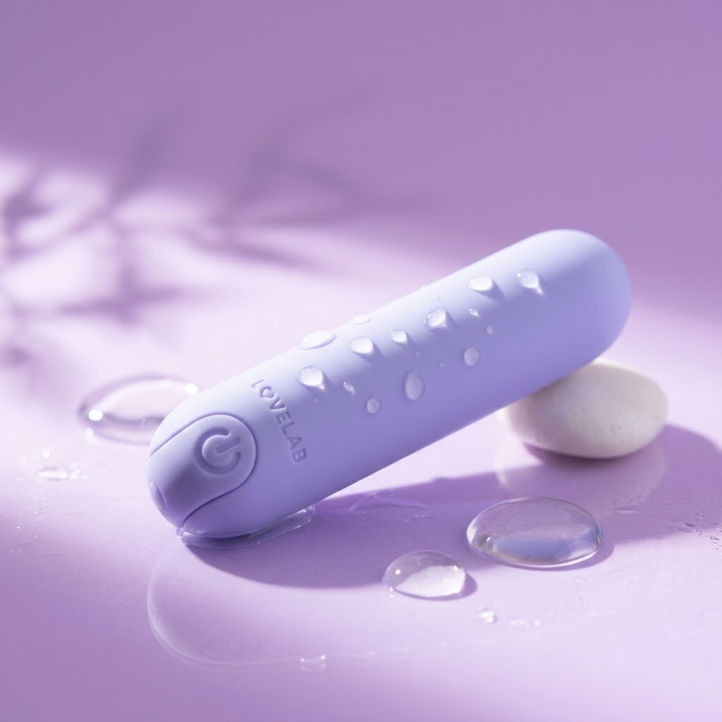 Lilac LoveLab Neo bullet vibrator with water droplets on a lilac surface