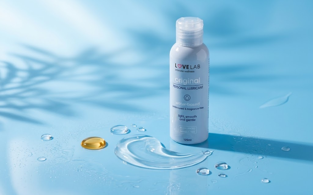 LoveLab Lube Original water-based lubricant bottle with clear gel and a drop of oil on a blue surface